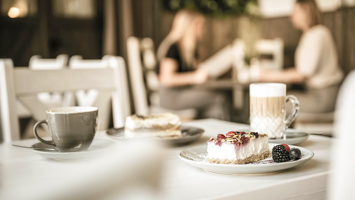 Tisch mit Kaffee und Kuchen im Vordergrund, im Hintergrund zwei Gäste mit Speisekarte im Farmhouse Cafe